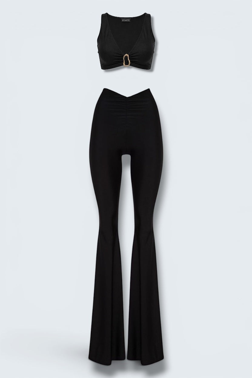 The Saint 54 Aphrodite black two-piece set with V-neck crop top, gold buckle detail, and flared trousers.