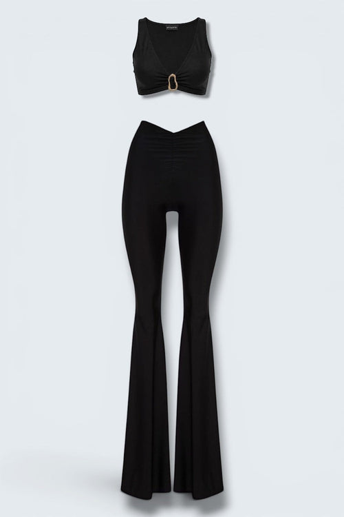 The Saint 54 Aphrodite black two-piece set with V-neck crop top, gold buckle detail, and flared trousers.