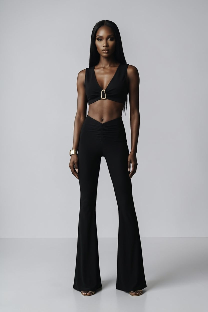 Model wearing The Saint 54 black Aphrodite set with V-neck crop top, gold hardware, and flared trousers.