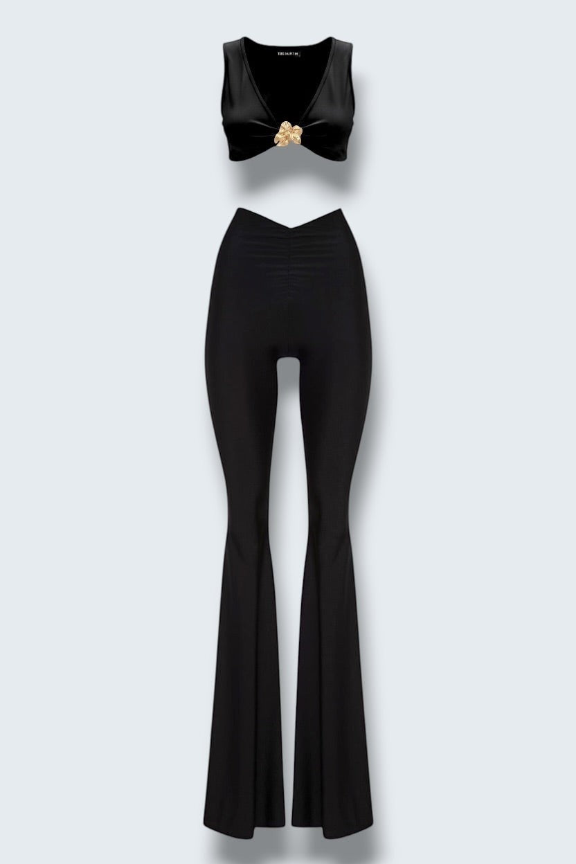 The Saint 54 black two-piece set featuring a cropped top with a gold accent and high-waisted flared wide-leg pants.