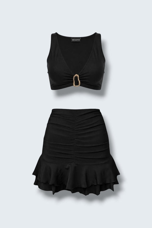 The Saint 54 black two-piece set featuring a fitted crop top with gold hardware and a ruched mini skirt with ruffles.