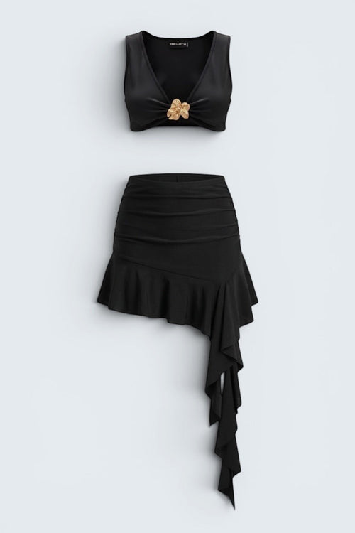 The Saint 54 black two-piece set featuring a fitted crop top with gold accent and an asymmetrical ruffled mini skirt.