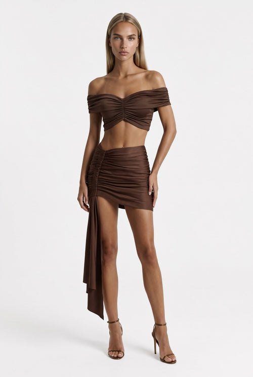 The Saint 54 brown two-piece set with off-shoulder gathered crop top and high-waisted mini skirt with side scarf
