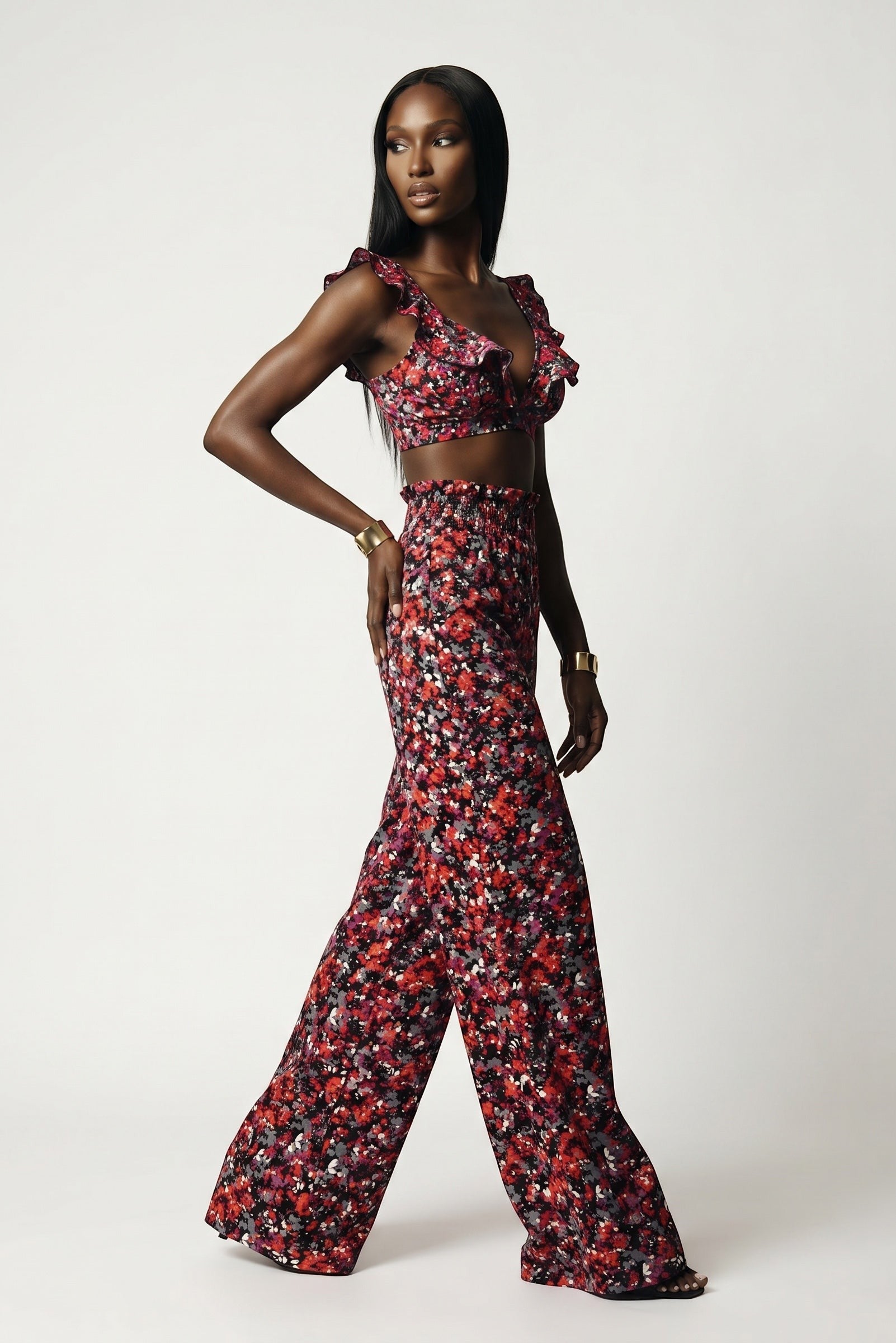 The Saint 54 Give&Shine floral print crop top with statement ruffles worn by a model with matching wide-leg trousers.