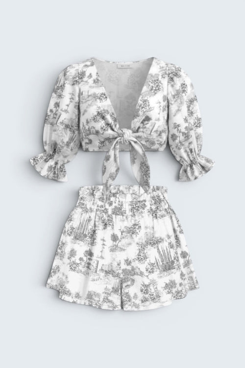 The Saint 54 grey and white toile print two-piece set with a tie-front puff sleeve top and ruffled high-waist shorts.