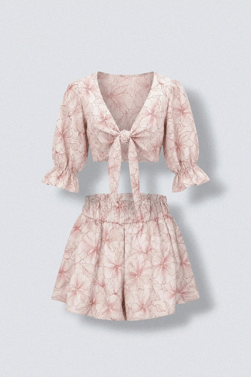 The Saint 54 pink floral print two-piece set featuring a tie-front puff sleeve crop top and ruffled high-waist shorts.